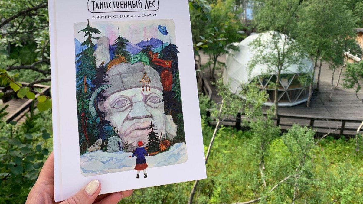 Женская рука держит книгу на фоне зелени летом.