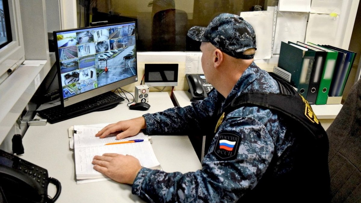Охранник сидит у монитора за столом.