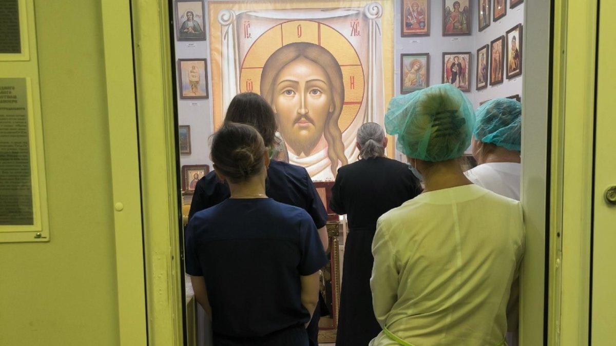 Люди стоят и смотрят на иконы в помещении.