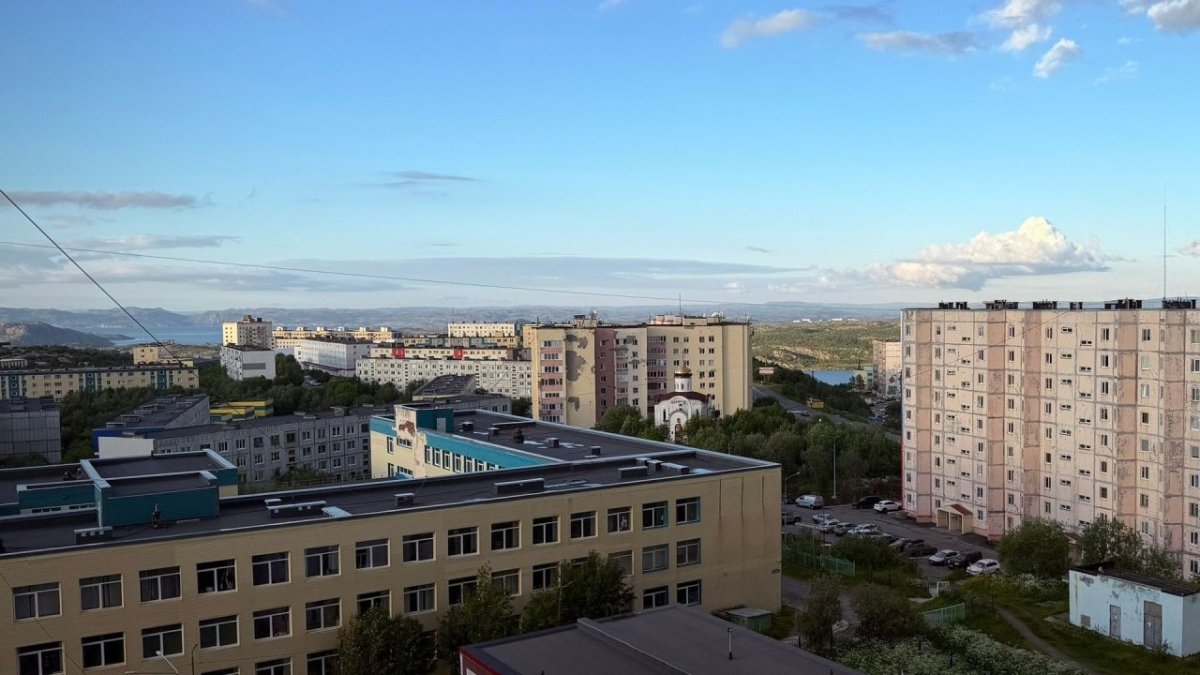 Множество домов на фоне летнего голубого неба и деревьев.