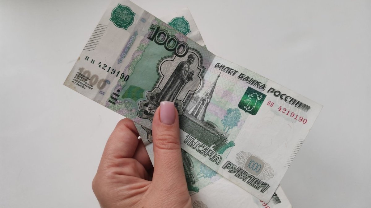 Две купюры номиналом в тысячу рублей держит женская рука.