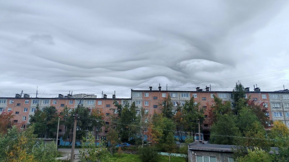 Волнообразные облака в пасмурном небе над домами города.