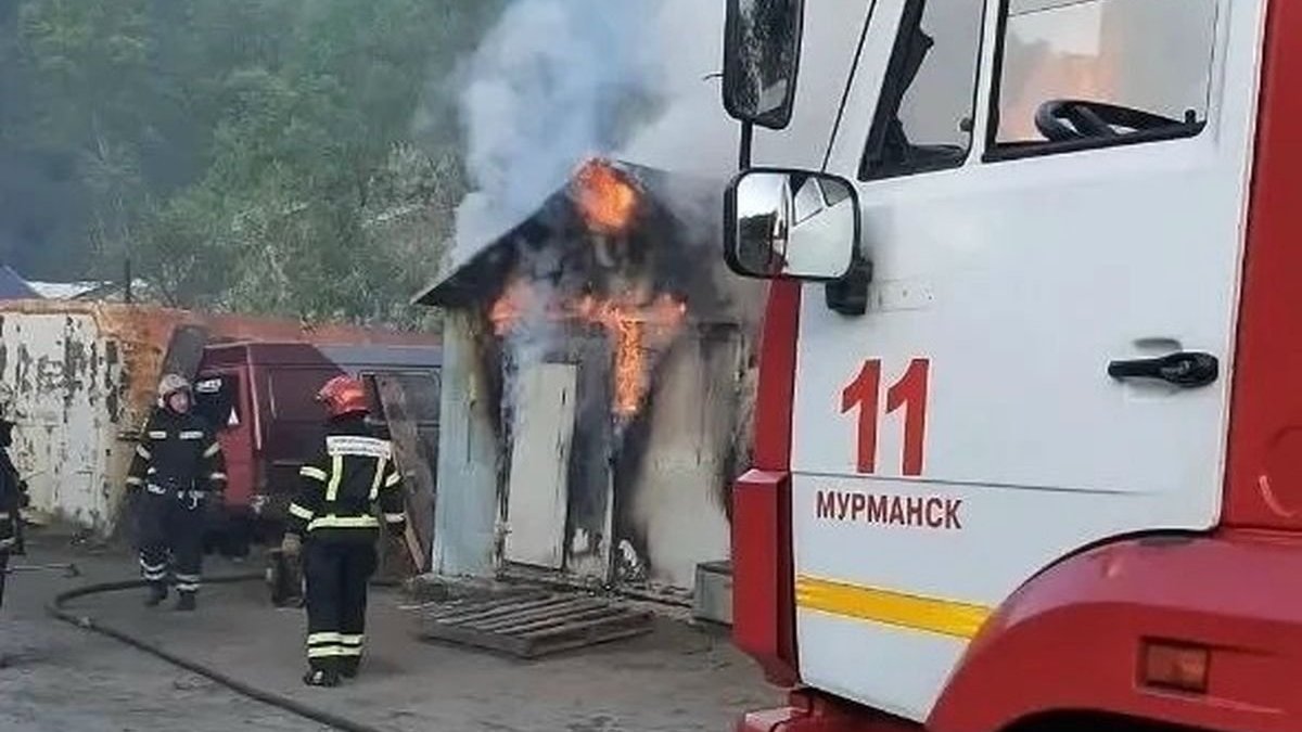 Пожарная машина и пожарные стоят рядом с горящим гаражом.