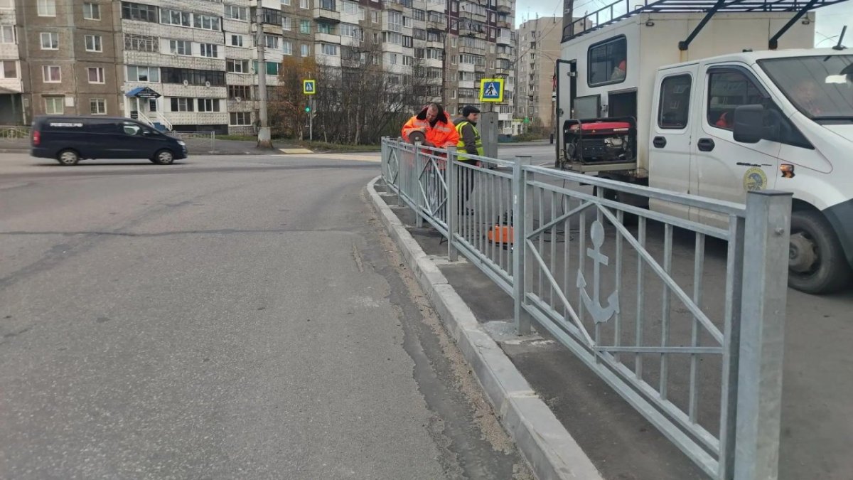 На улице в городе специалисты чинят забор.