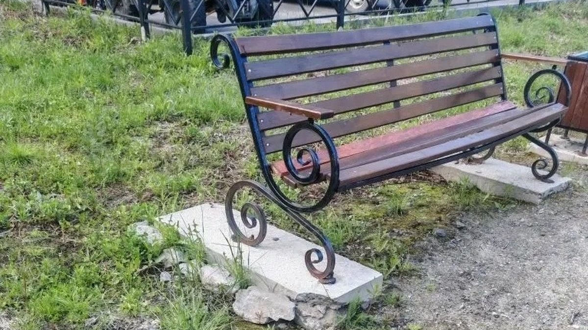 Скамейка стоит на бетонных подставках на траве.