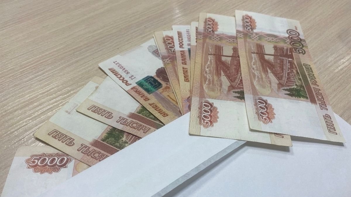 Купюры номиналом в пять тысяч рублей лежат рядом с белым конертом на столе.